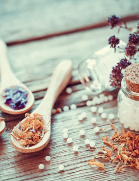 Bottle of white homeopathy globules wooden spoons and dry healthy herbs. Selective focus. Retro styled.